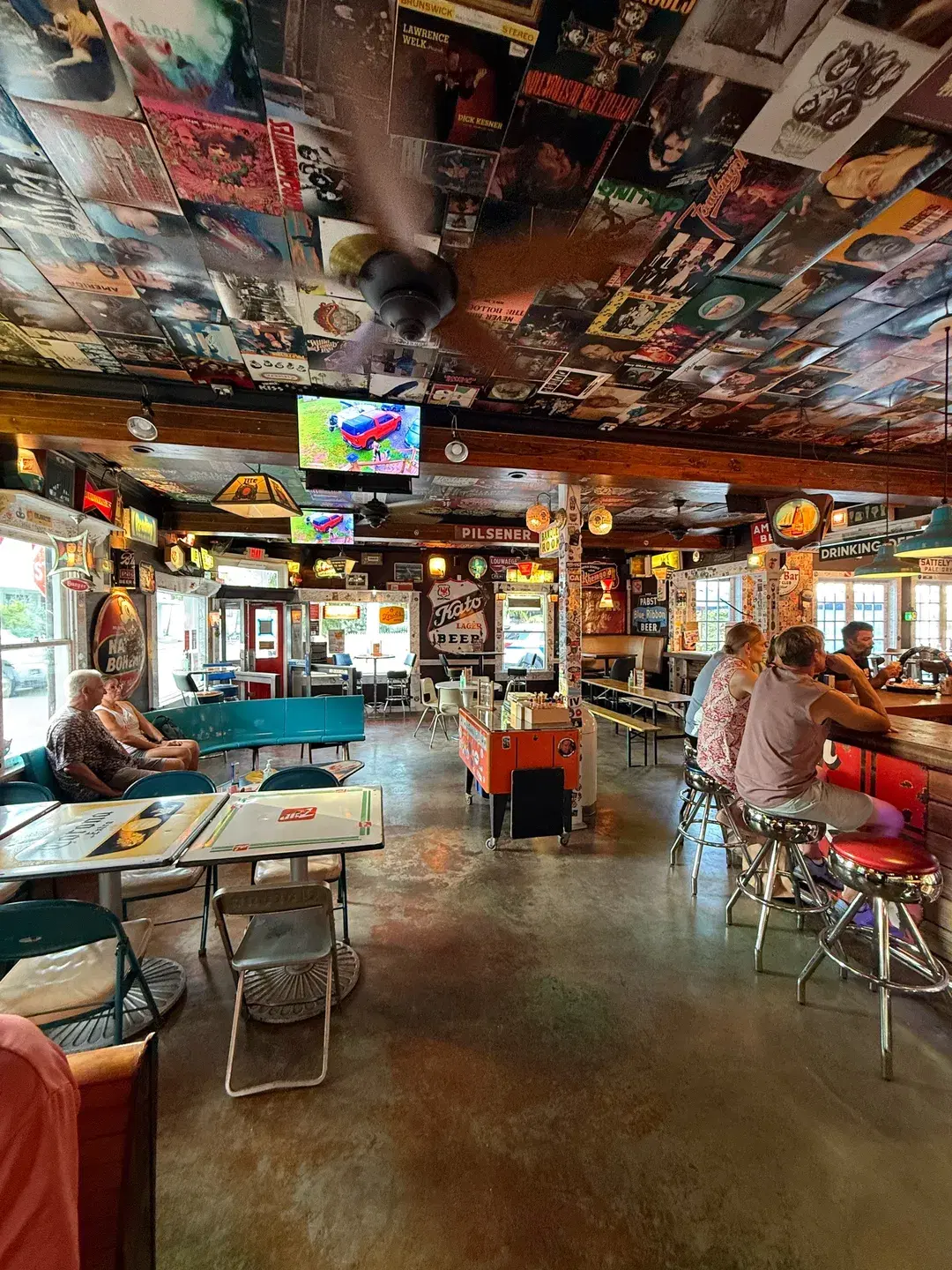 Dining area at The Dive Bar Shirt Club with a ceiling covered in vintage album covers, vintage furniture, and a ceiling fan