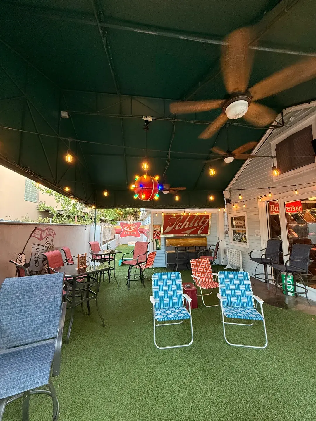 Covered outdoor patio at The Dive Bar Shirt Club with string lights, artificial turf, and a vintage 'Schlitz' sign