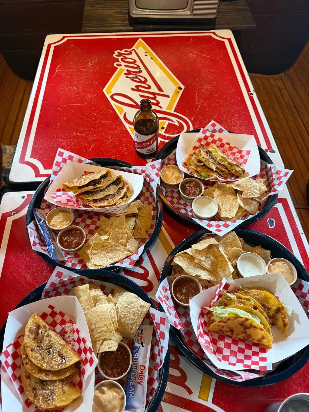 Overhead view of taco plates, tortilla chips, salsa, and a Red Stripe beer on a vintage diner-style table